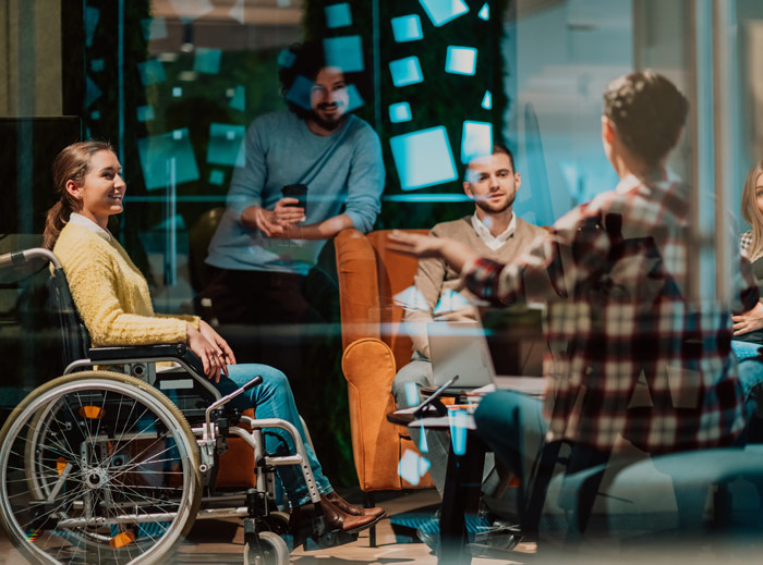 group discussion including three people interacting a woman in a wheelchair smiling while others listen attentively in a modern workspace